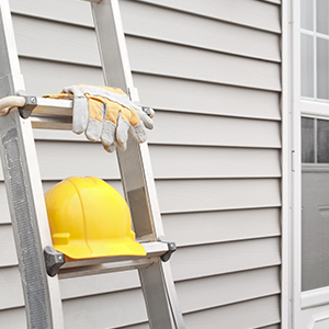 Ladder with a hard hat and gloves next to gray home siding